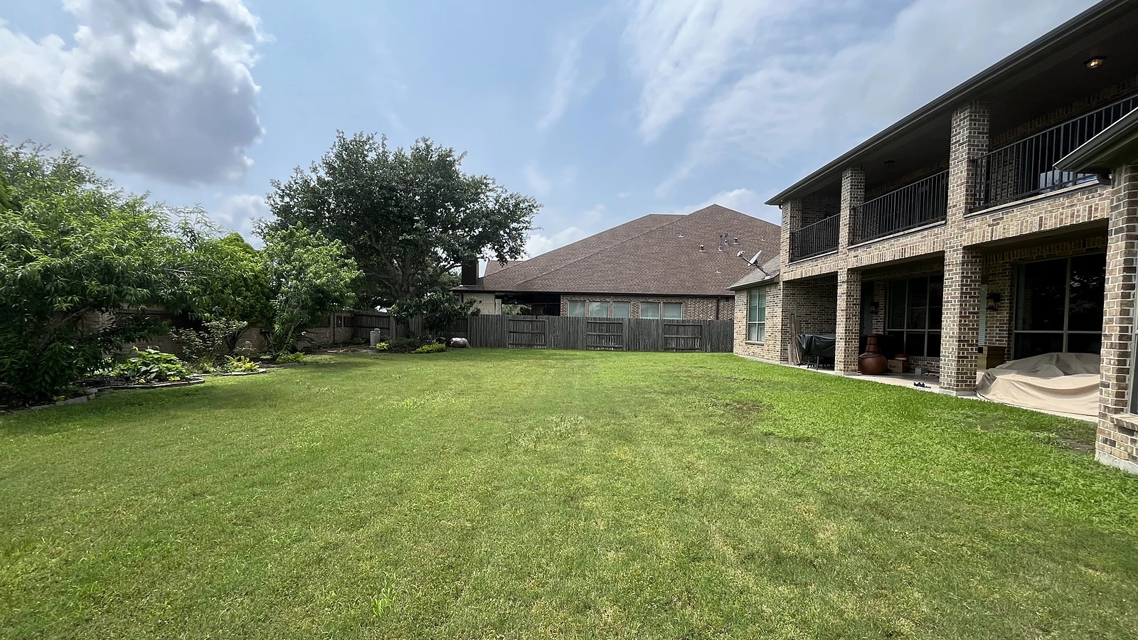 Open backyard lawn before Bager's outdoor living project in Cinco Ranch, Katy, TX — the two-story brick home with a bare covered patio and empty yard