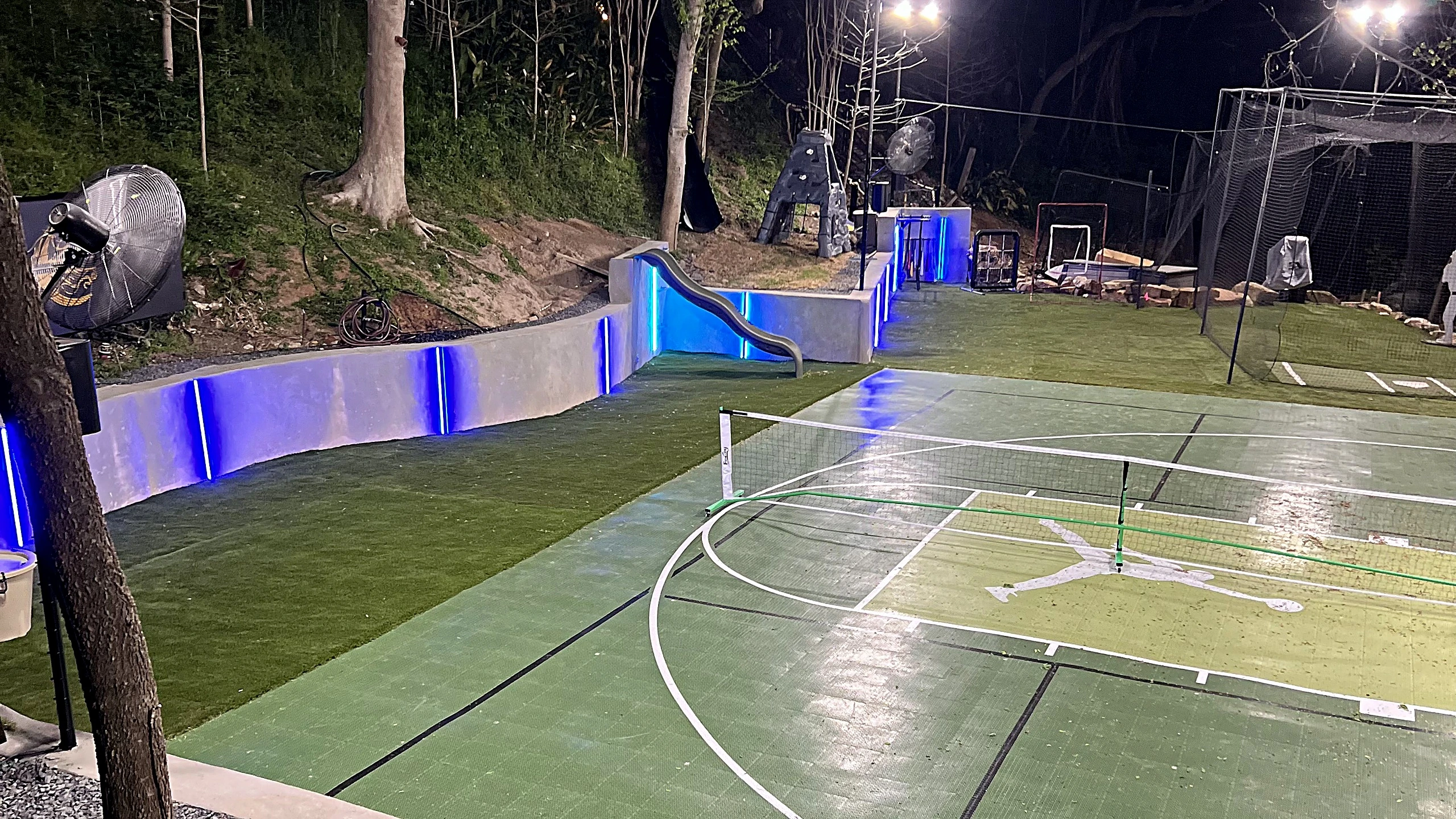Basketball goal and training area visible on synthetic turf upper level behind sport court surface