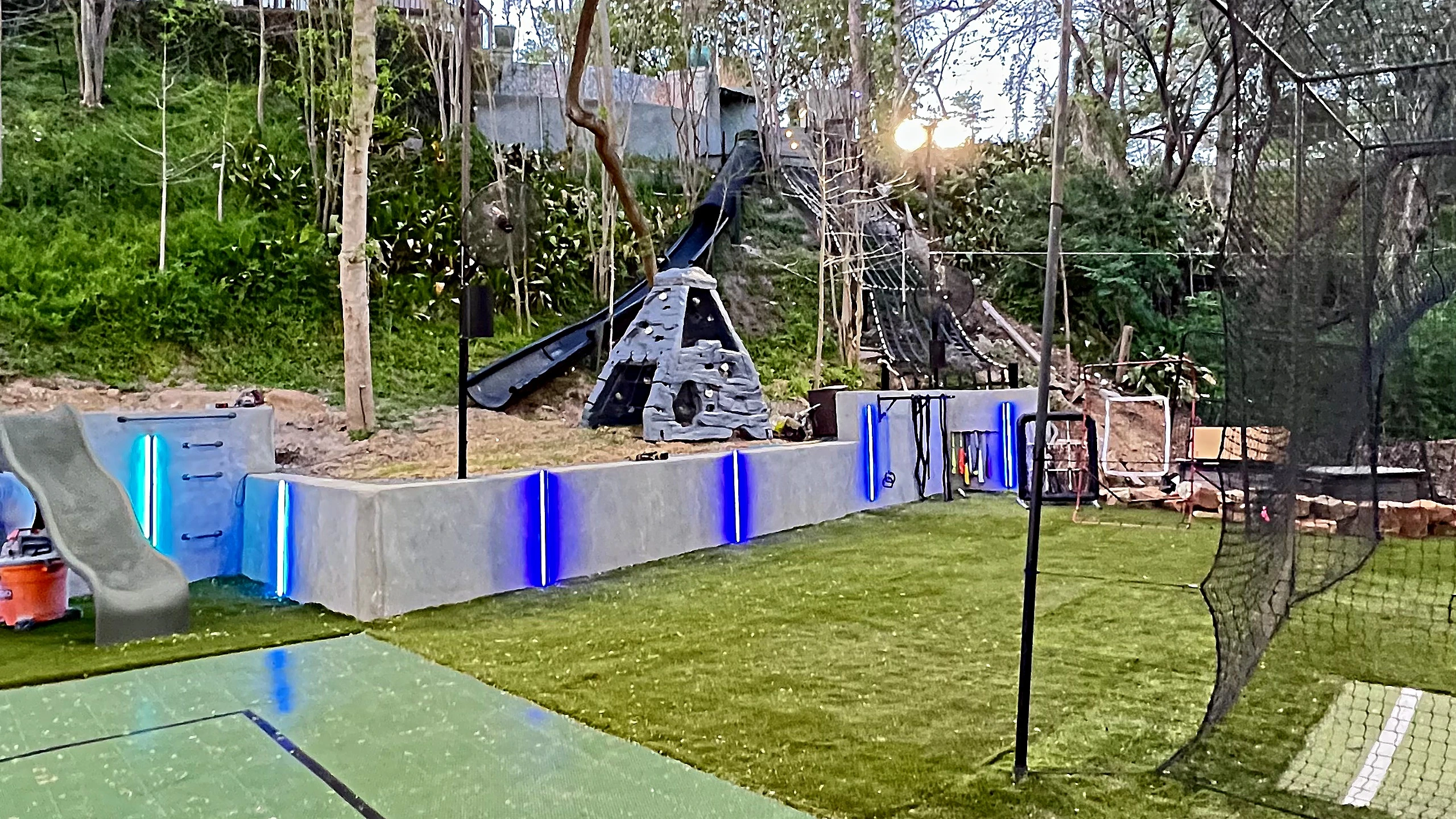 Overhead night view of flood-lit multi-sport court beside LED-accented terraced retaining walls
