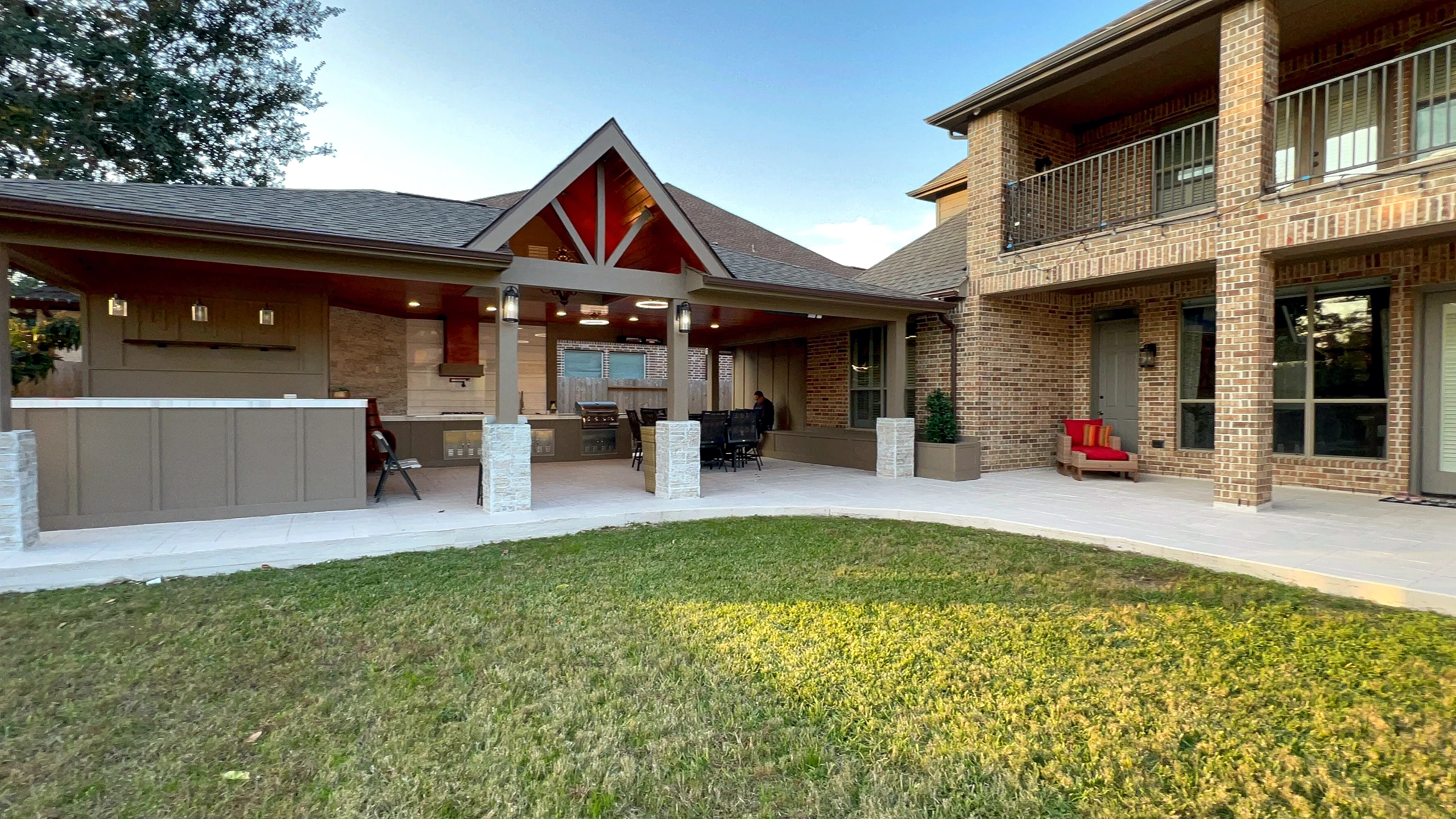 Completed covered outdoor kitchen pavilion with stone columns, stained wood ceiling, and bar counter extending from Cinco Ran