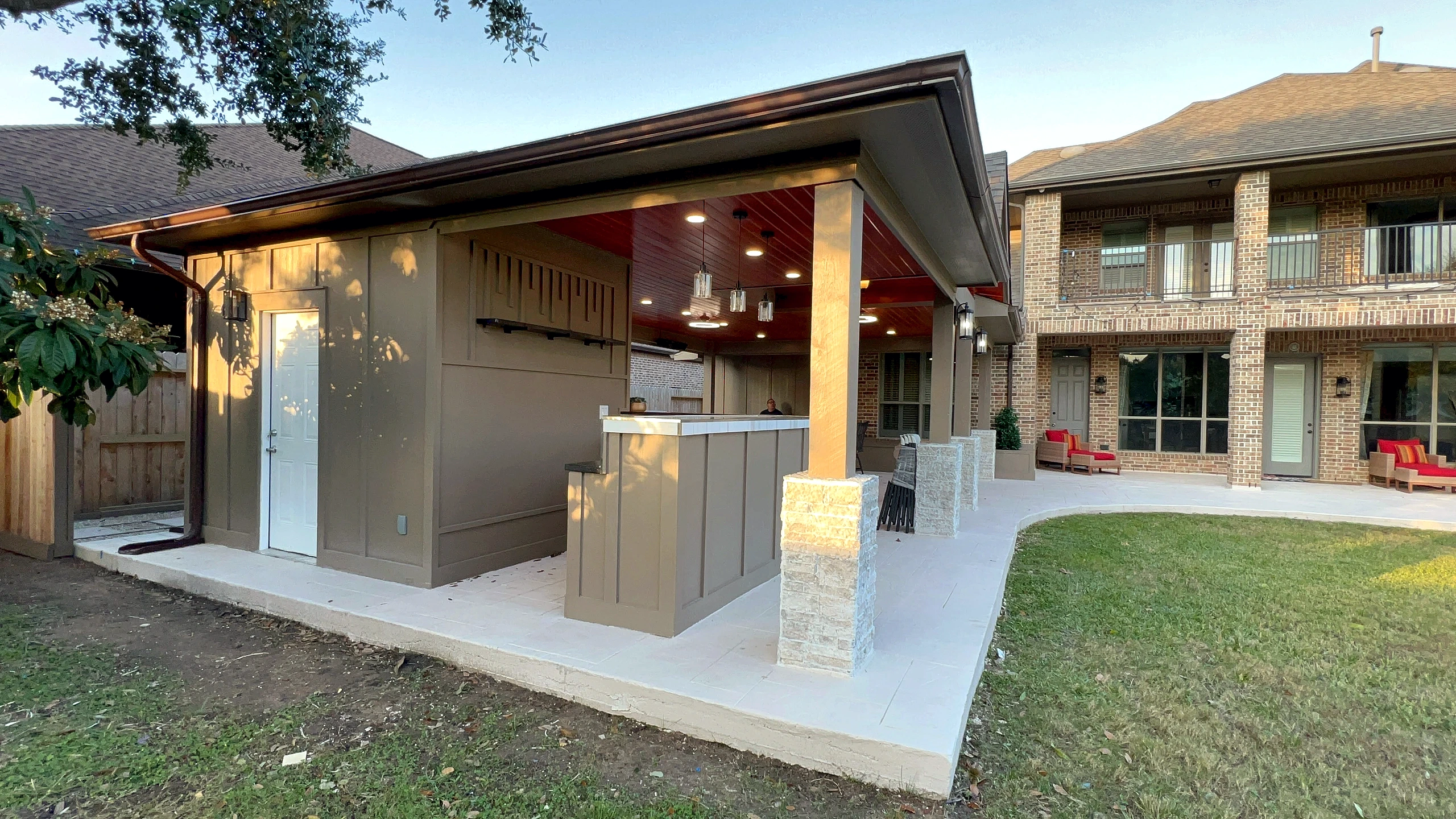 Side elevation of outdoor pavilion addition with board-and-batten utility room, stone-clad bar counter, and wood ceiling at g