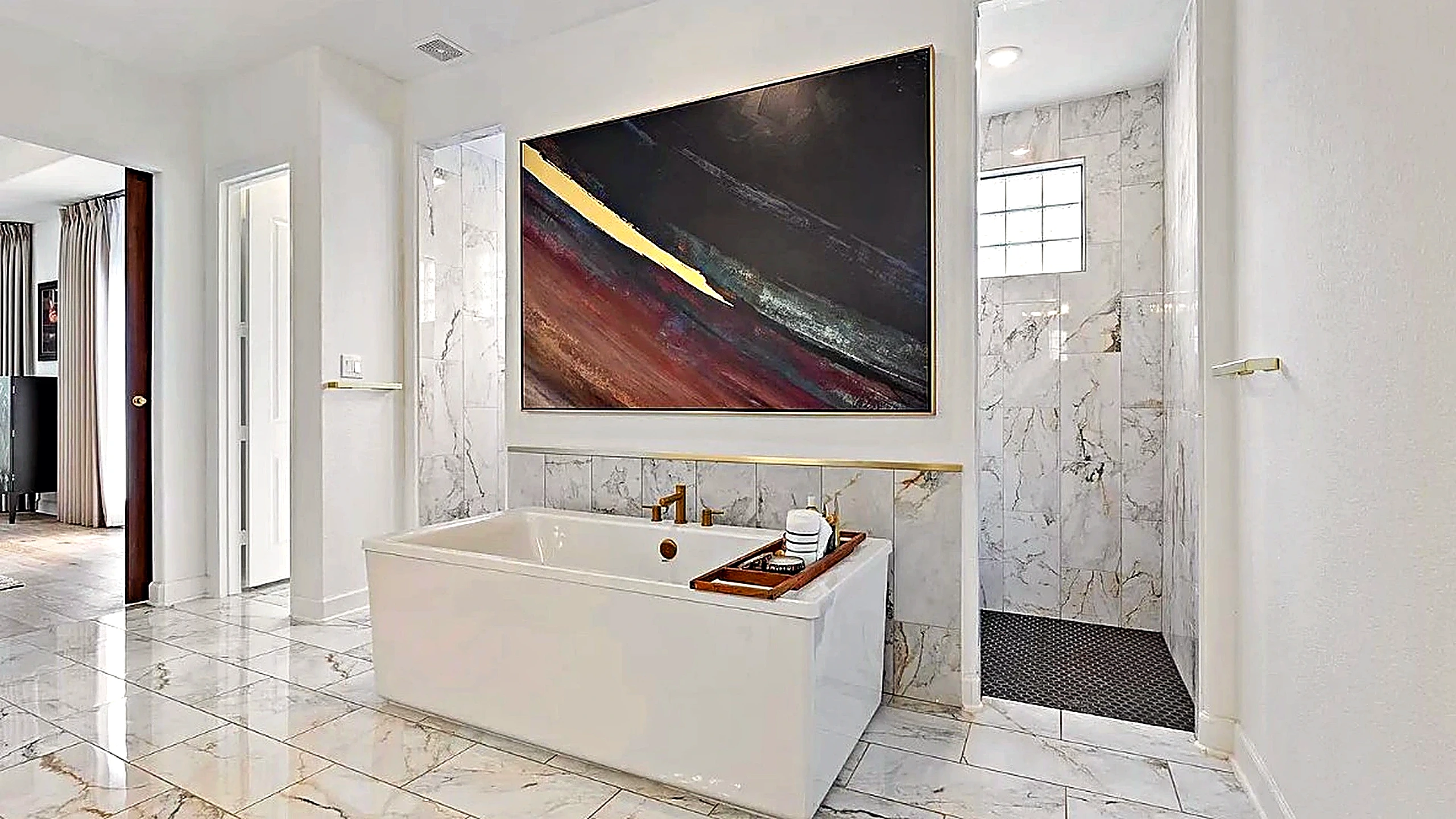 Freestanding white soaking tub, brass hardware, veined stone walls, and abstract canvas — primary bathroom remodel, The Woodl