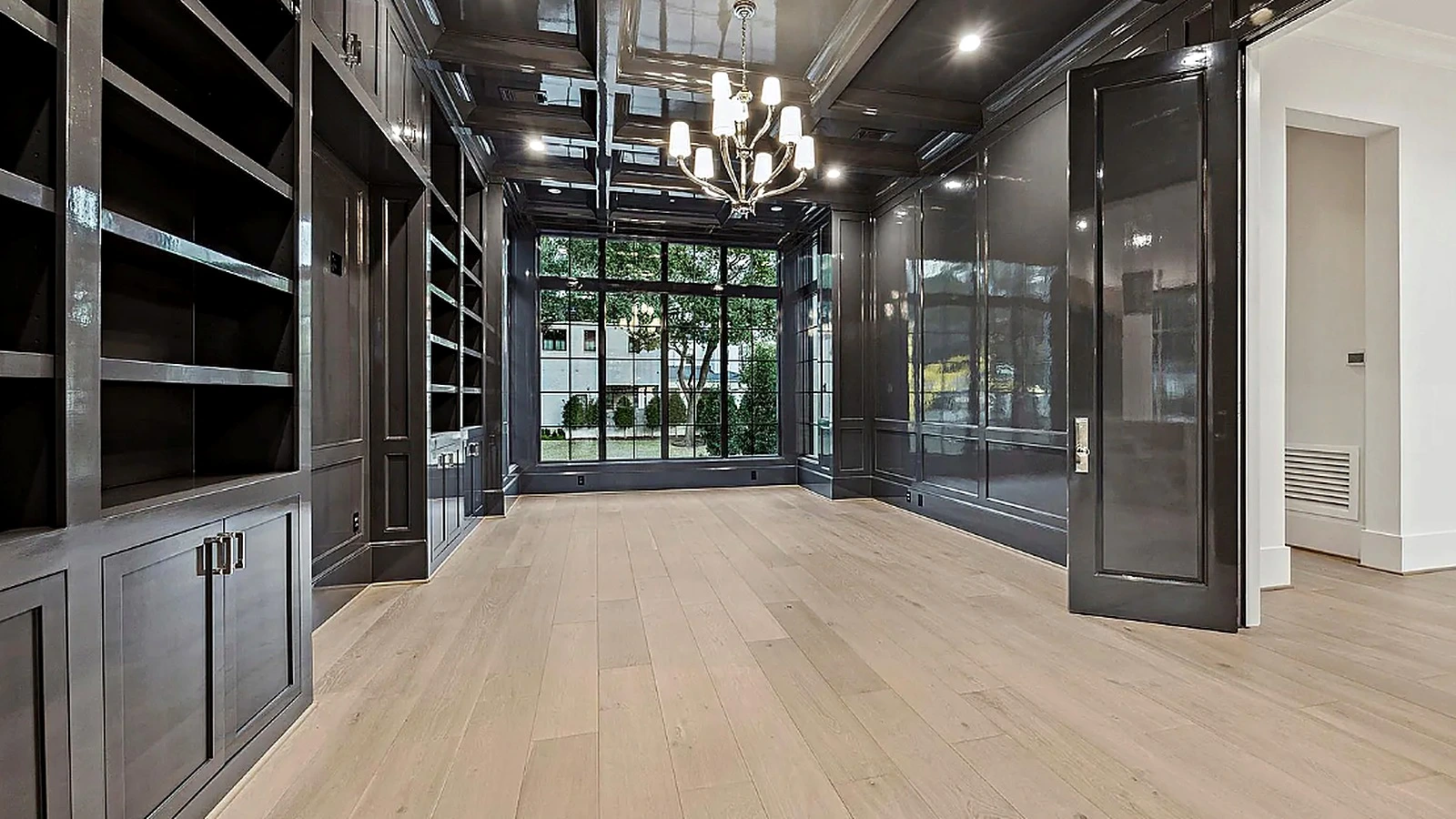 Backlit wood-and-metal wine racking behind glass-and-steel doors set into an exposed brick wall