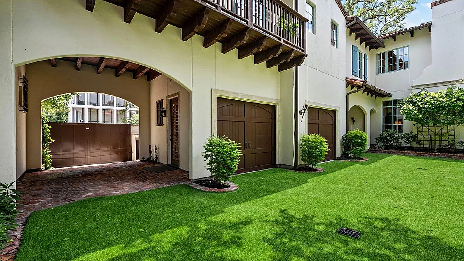 Side elevation showing arched carport, exposed timber bracket eaves, and wood garage doors on repainted stucco home