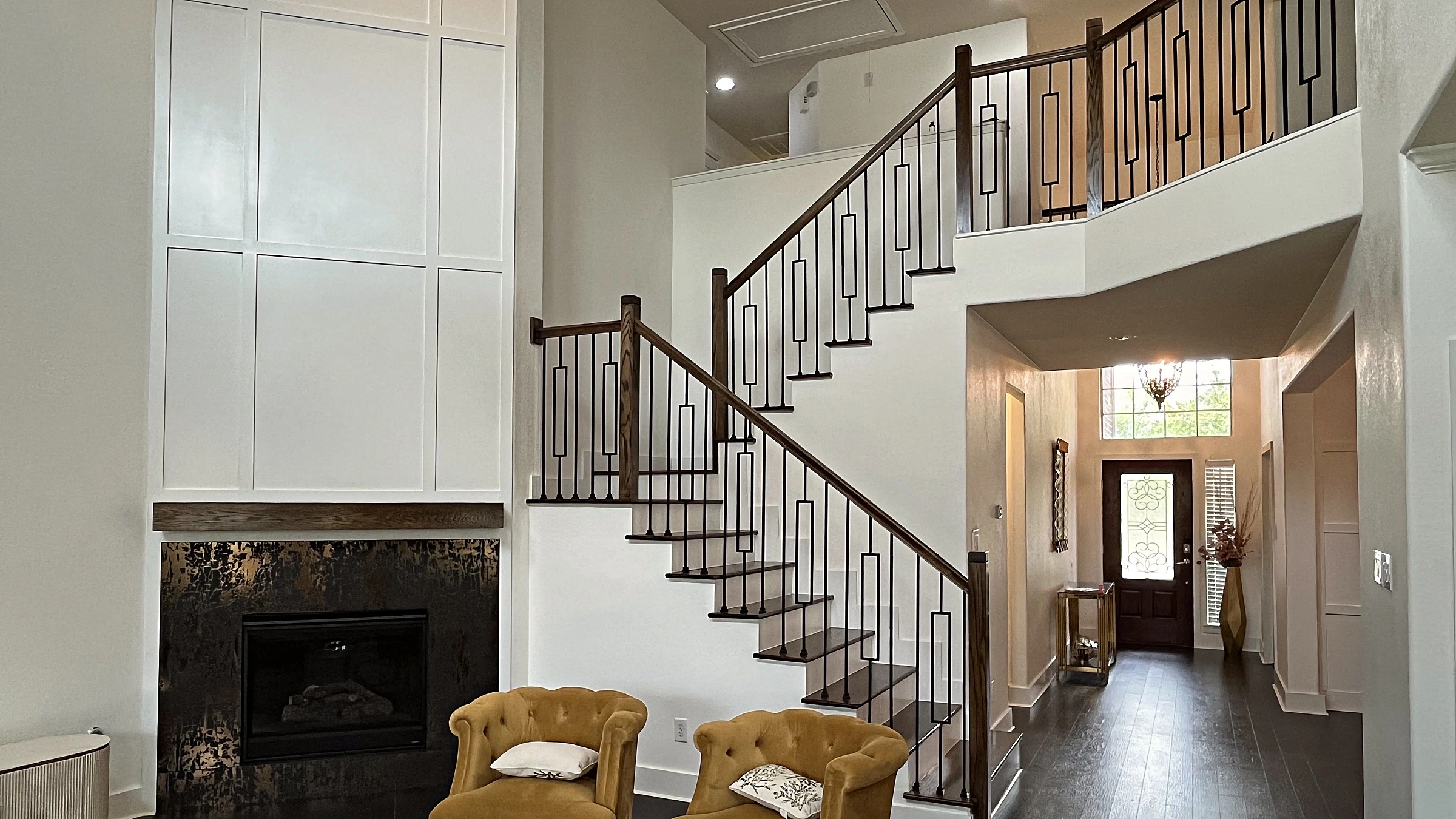 Remodeled Fulshear living room with two-story painted paneling, floating wood mantel, textured tile surround, and dark stair