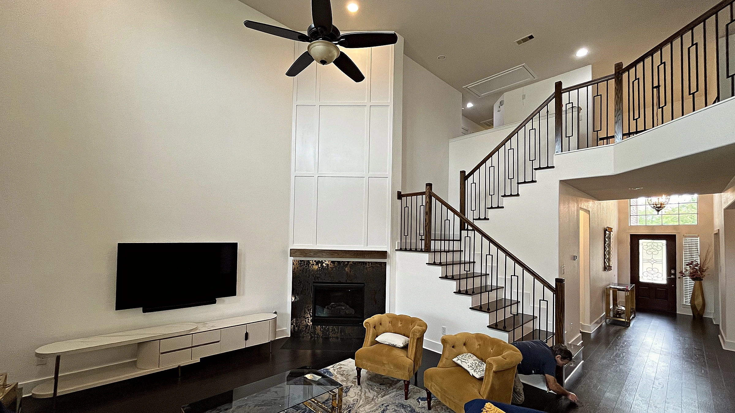 Upper landing railing with dark-stained wood handrail and rectangular iron balusters overlooking two-story living space
