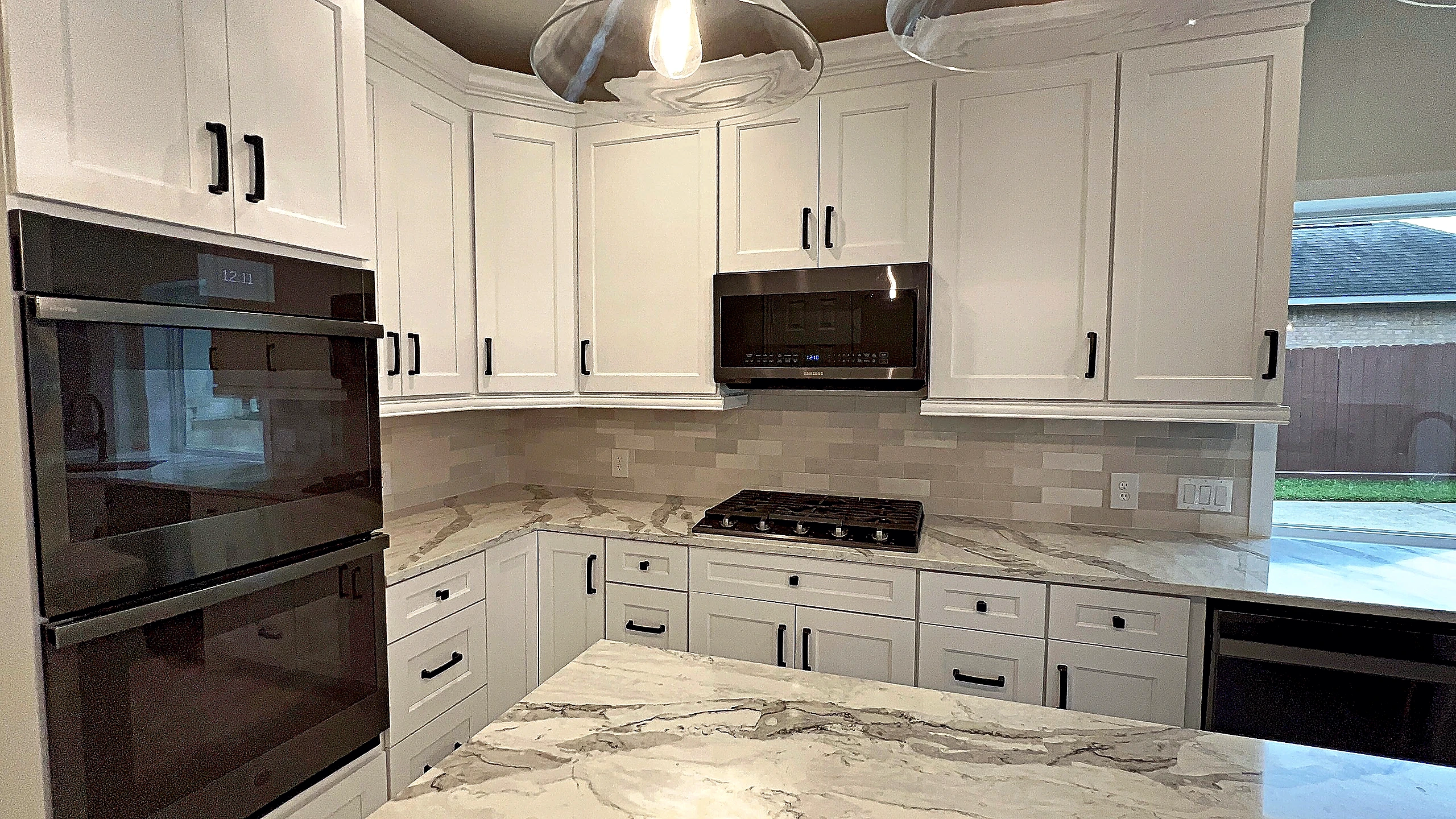 White raised-panel cabinetry with crown molding, matte black hardware, and double wall oven in a Houston kitchen remodel