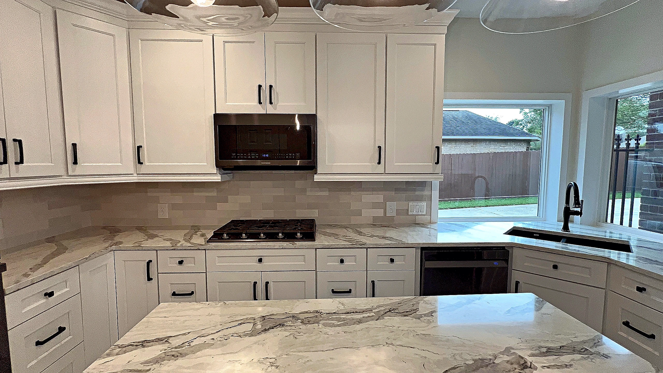 Full kitchen view with natural stone island, staggered tile backsplash, and gas cooktop — Spring Valley Village remodel by Ba