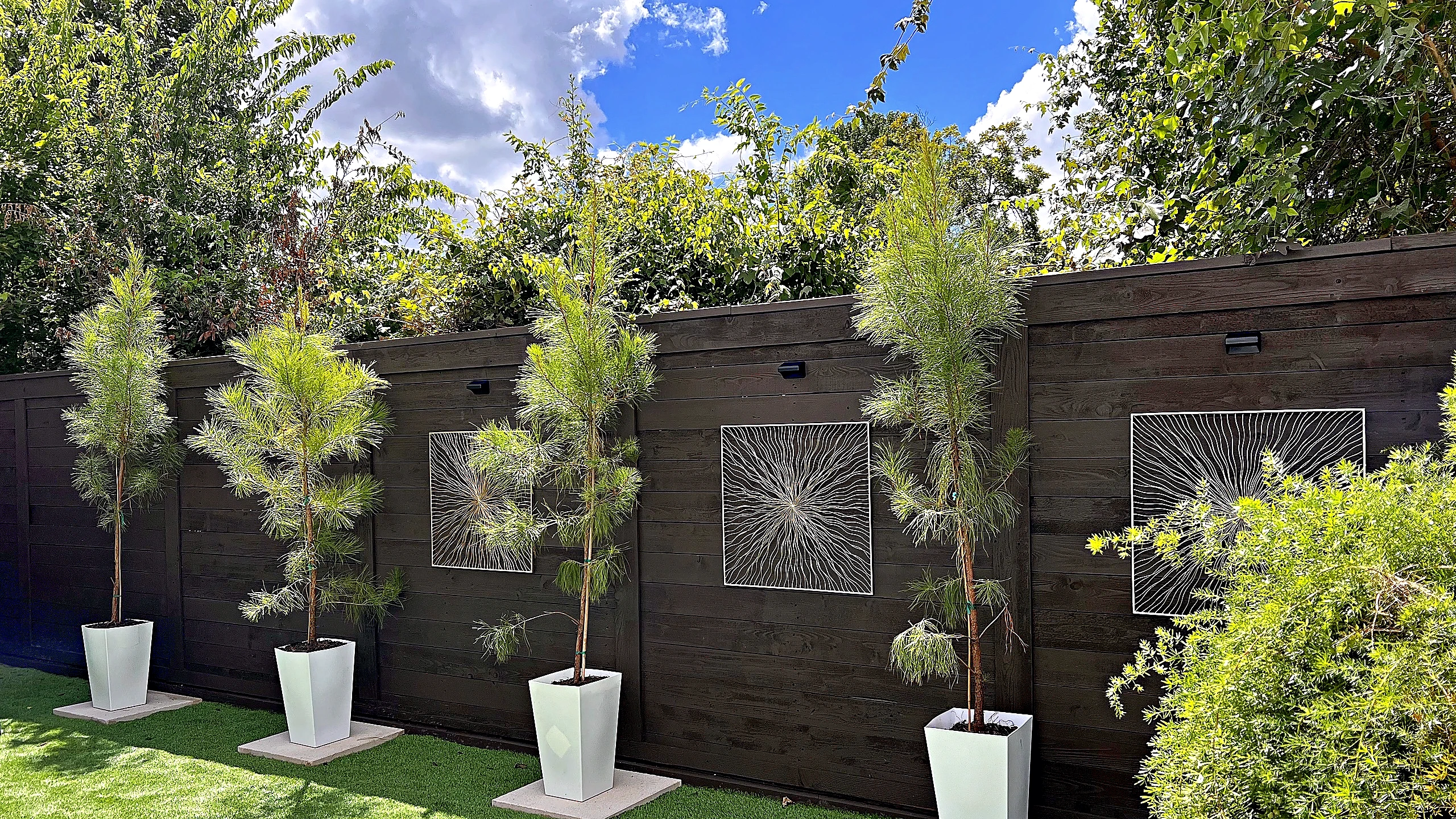 Finished courtyard with dark-stained wood fence, metal wall panels, white planters, and synthetic turf in Spring Valley Villa