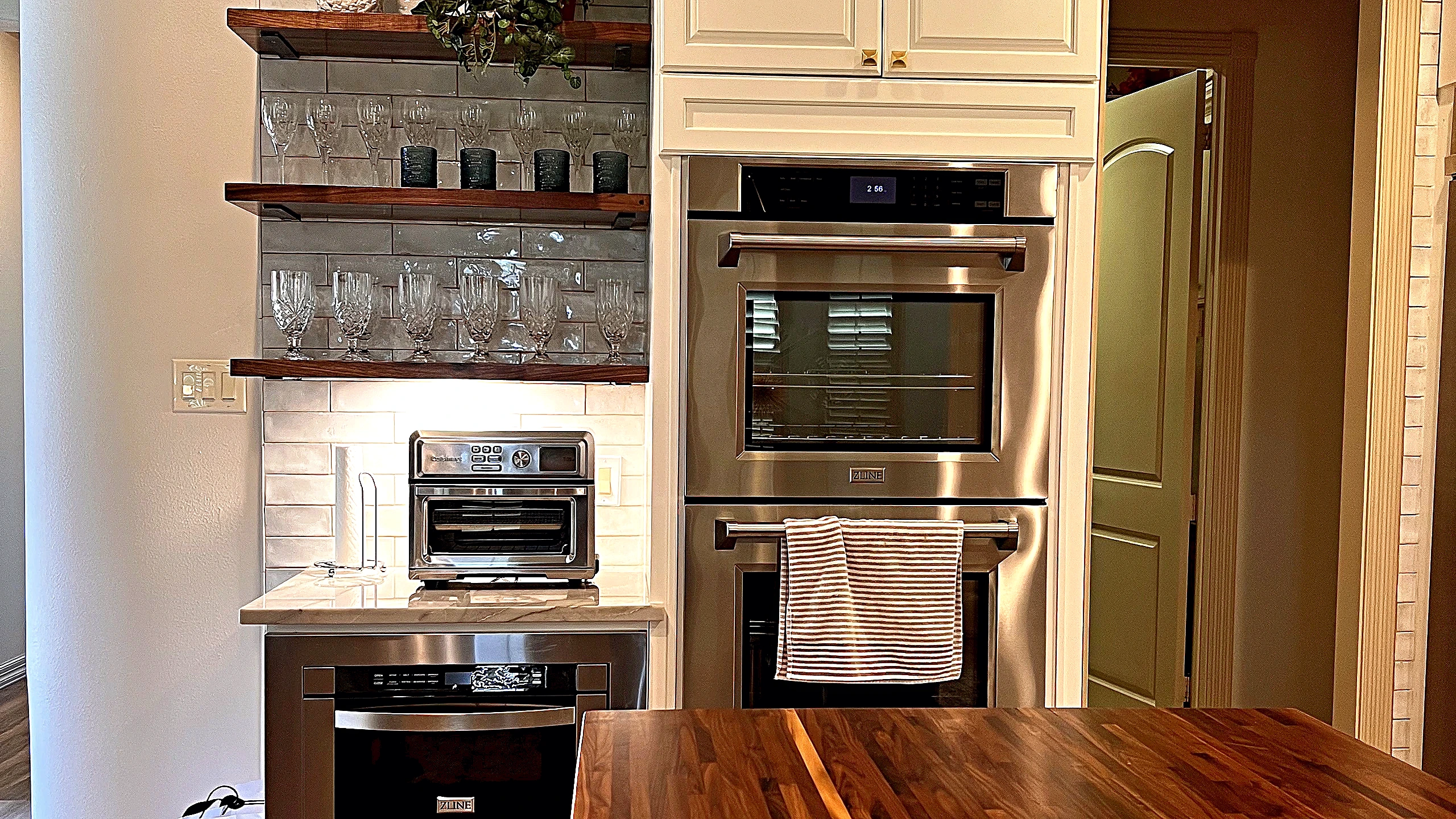 Wide kitchen view showing glazed tile, open shelving, and white cabinetry in Tomball residence