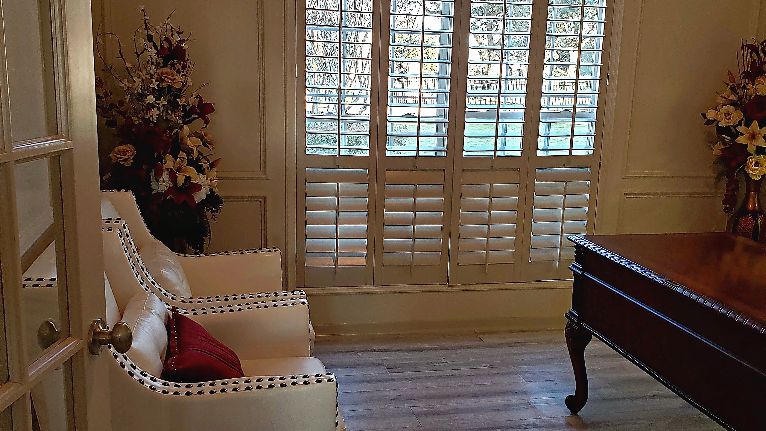 Renovated interior sitting room in Tomball featuring wood plank flooring, panel molding walls, and plantation shutters